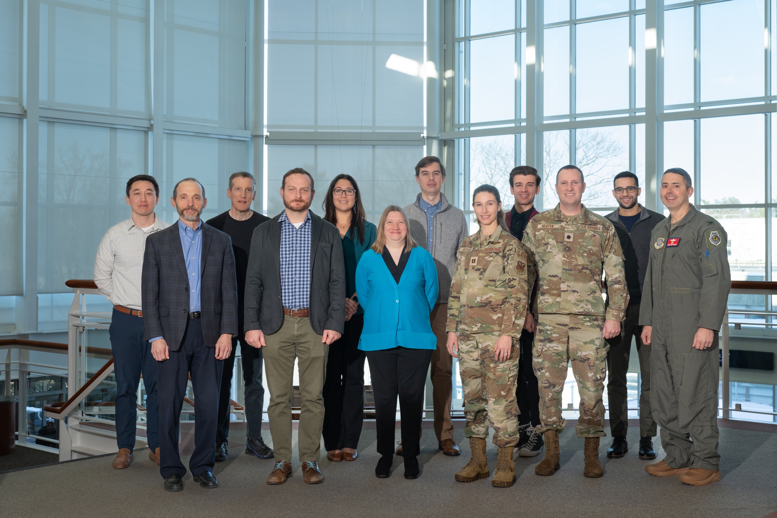A group of 12 people representing the 618th AOC and Lincoln Laboratory pose for a group photo in the Laboratory lobby.