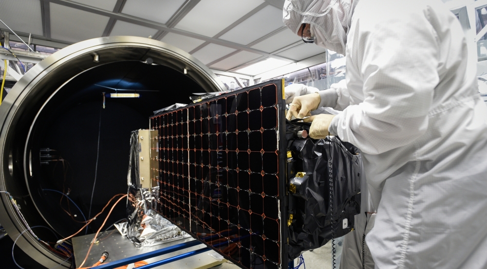 A researcher, wearing a head-to-toe covering to avoid contaminants, makes adjustments to a satellite before loading it into an environmental test chamber.