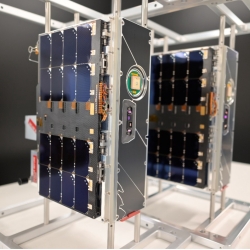 Two CubeSats (roughly 20 x 10 x 30 cm in size) are shown in a lab setting 