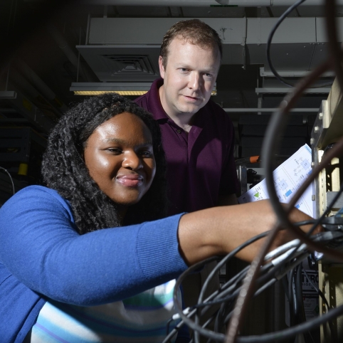 Derrick Feld looks on as AFCEA intern Chi-chi Nwodoh connects wires on the test terminal she helped build.