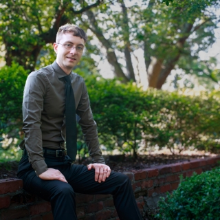 Connor Mathews sits outside on a brick wall 