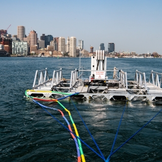 A metal frame floats in Boston Harbor, with the city in the backdrop.