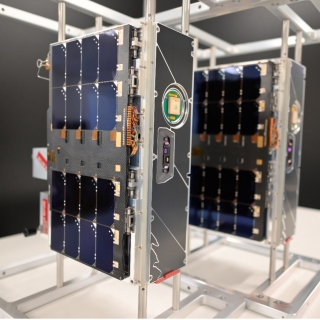 Two CubeSats (roughly 20 x 10 x 30 cm in size) are shown in a lab setting 